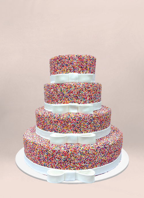 Photo: four tiered rainbow sprinkle covered cake with fondant white ribbon on each tier