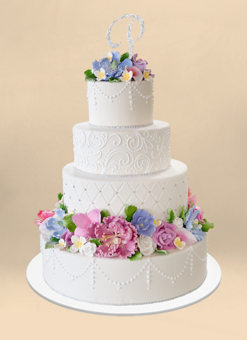 Photo: beautiful white cake with piped patterns on each tier, colorful cugar flowers